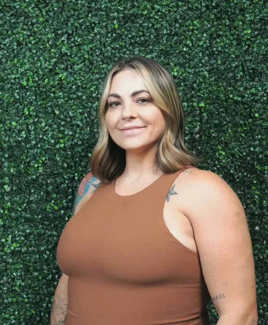 Jennifer, founder and stylist at JM Salon Palm Beach, in front of a wall of green leaves