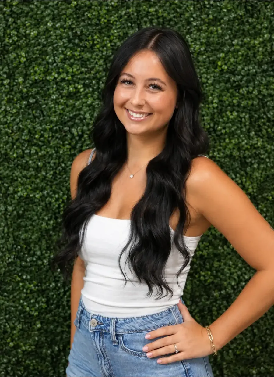 Olivia, stylist at JM Salon Palm Beach, in front of a wall of green leaves