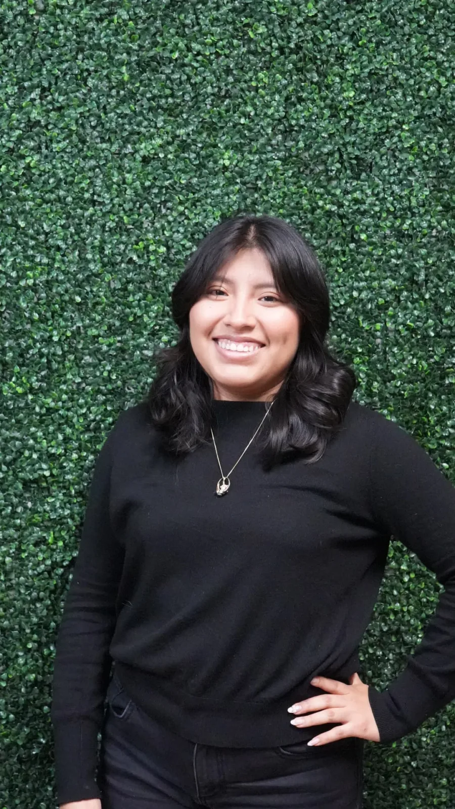 Rubi, stylist at JM Salon Palm Beach, in front of a wall of green leaves